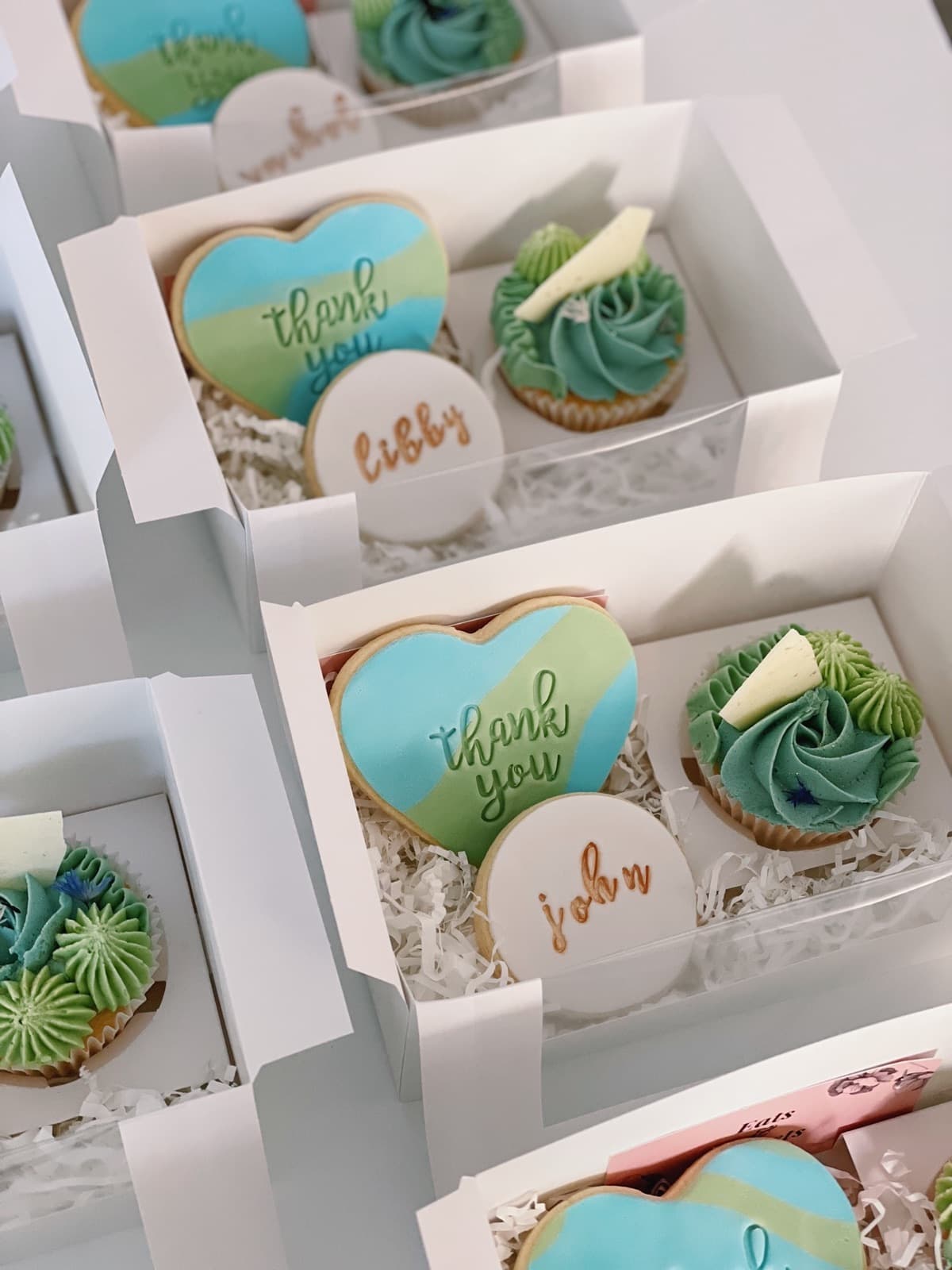 An open gift box of iced cookies and cupcakes, packed in rows and tied for giving.