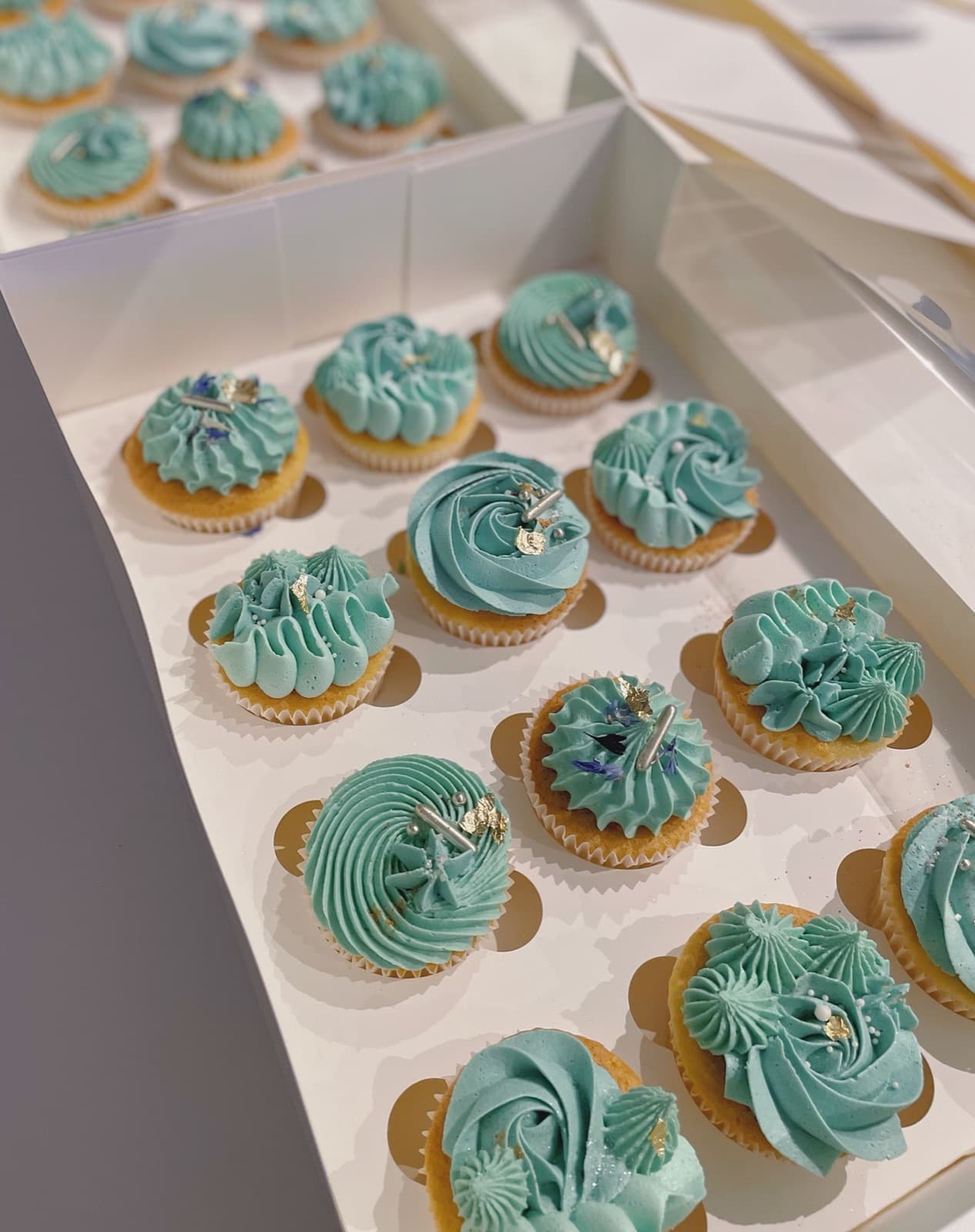 Cupcakes piped with tall teal buttercream swirls, finished with gold sprinkles.