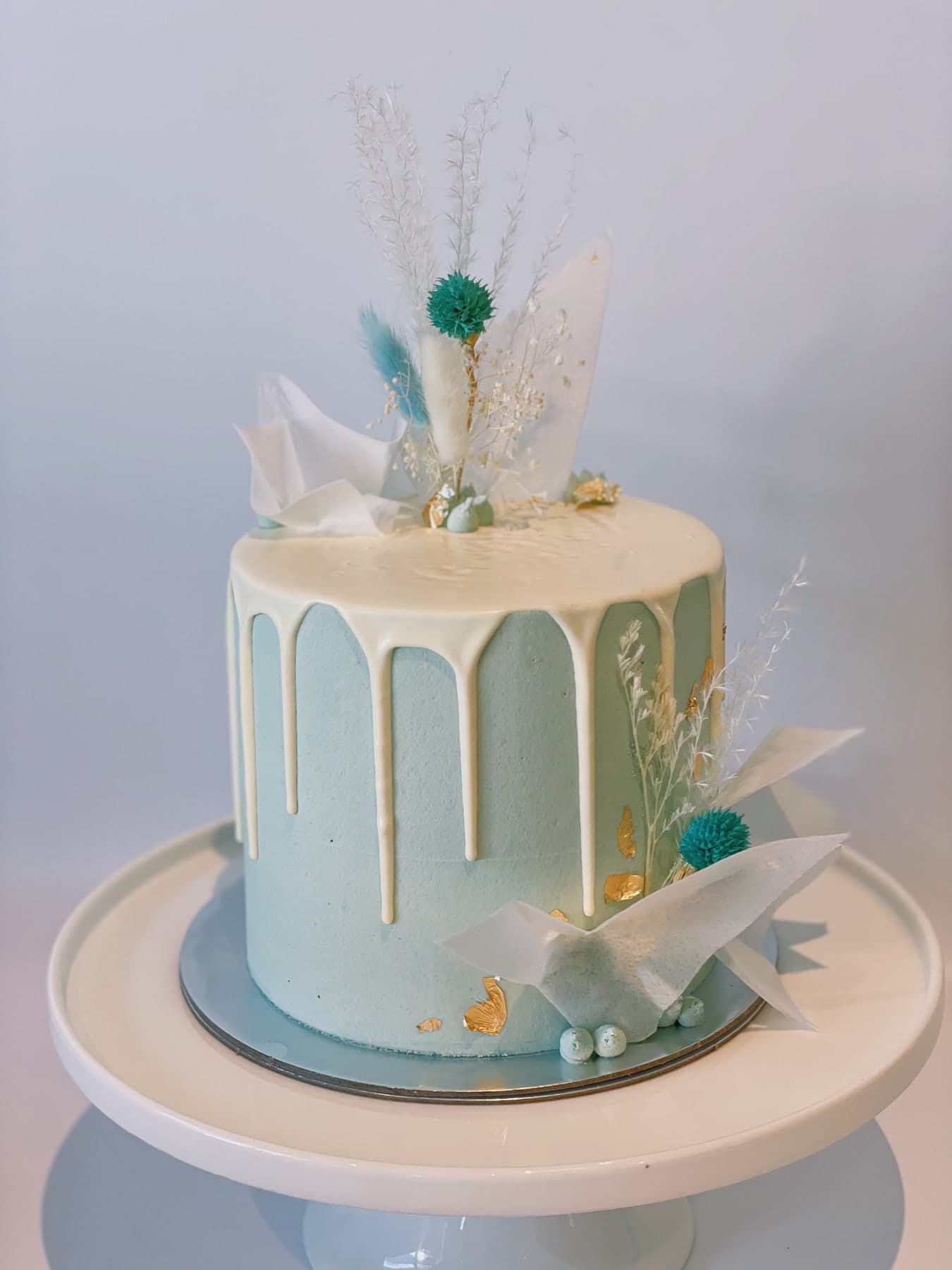 A pale blue cake with a white drip, rice-paper sails, dried flowers and flecks of gold leaf.