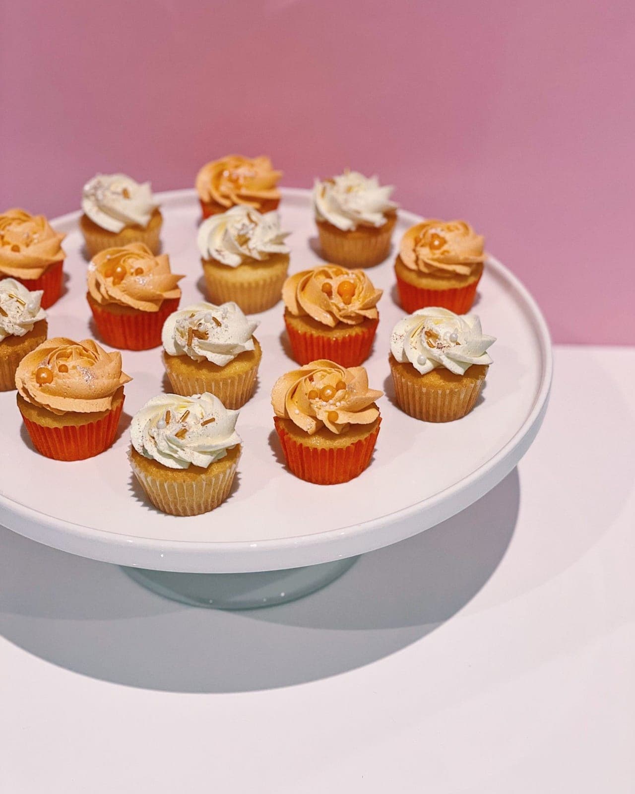Mini cupcakes on a white stand, orange rosettes in orange cases alternating with white swirls, finished with pearl sprinkles.