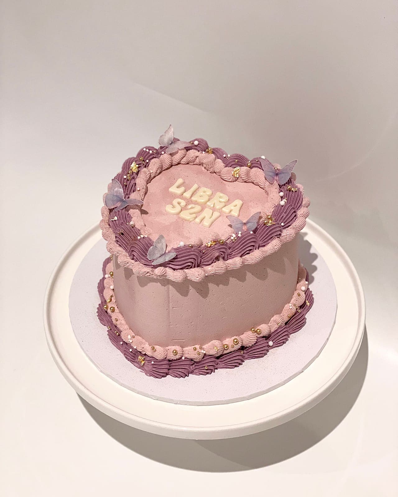 A heart-shaped cake in pale pink with lilac vintage piping, little butterflies and a star-sign message piped on top.