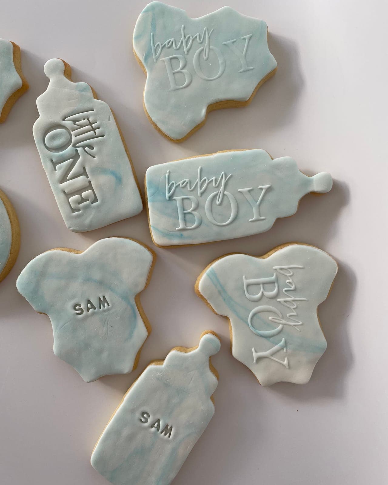 Bottle and onesie cookies topped with blue marbled icing and embossed with baby-boy messages.